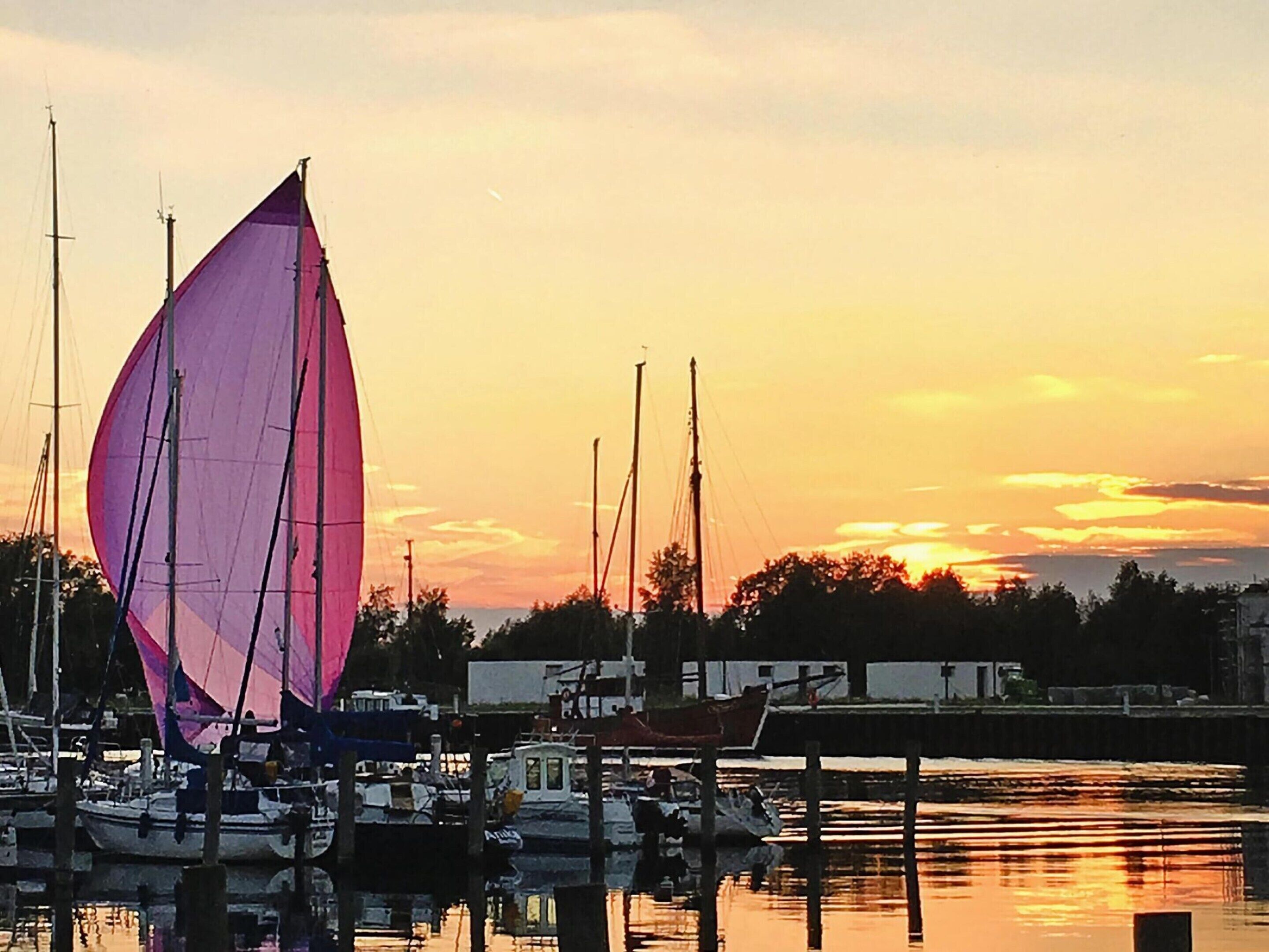 A marina with sailboats docked at wooden piers, calm water reflecting the sunset.