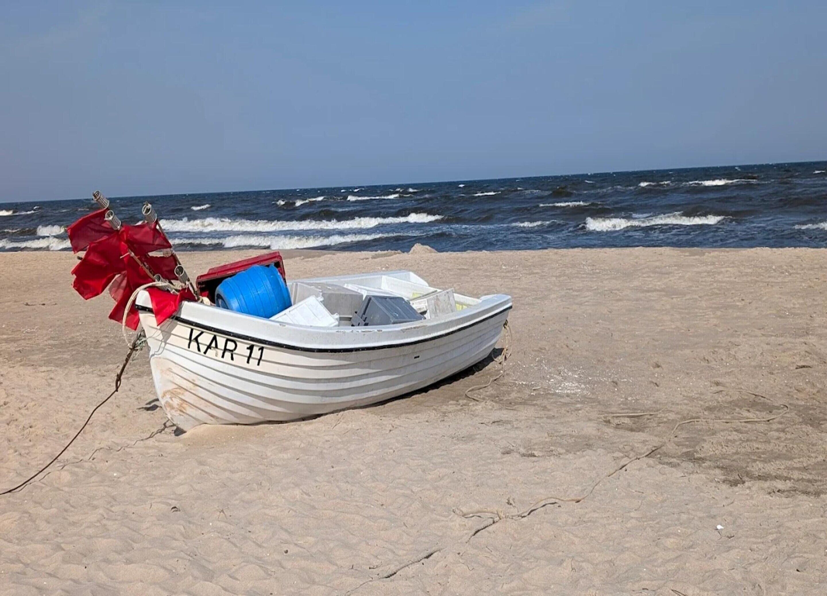 Un petit bateau blanc portant le numéro « 11 », sur une plage de sable, avec l’océan en arrière-plan.