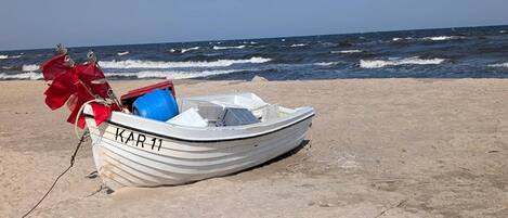 Un petit bateau blanc portant le numéro « 11 », sur une plage de sable, avec l’océan en arrière-plan.
