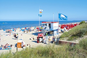 A beach with a lifeguard tower, beach umbrellas, and people sunbathing. - Appartementhaus in Trassenheide (Trassenheide)