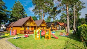 Um parquinho com estruturas de lazer coloridas e cabanas de madeira numa área arborizada.