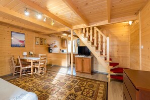 A wooden cabin interior with a dining area, kitchen, and a staircase.