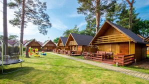 Fileira de cabanas de madeira com varandas, cercada por um gramado e árvores.