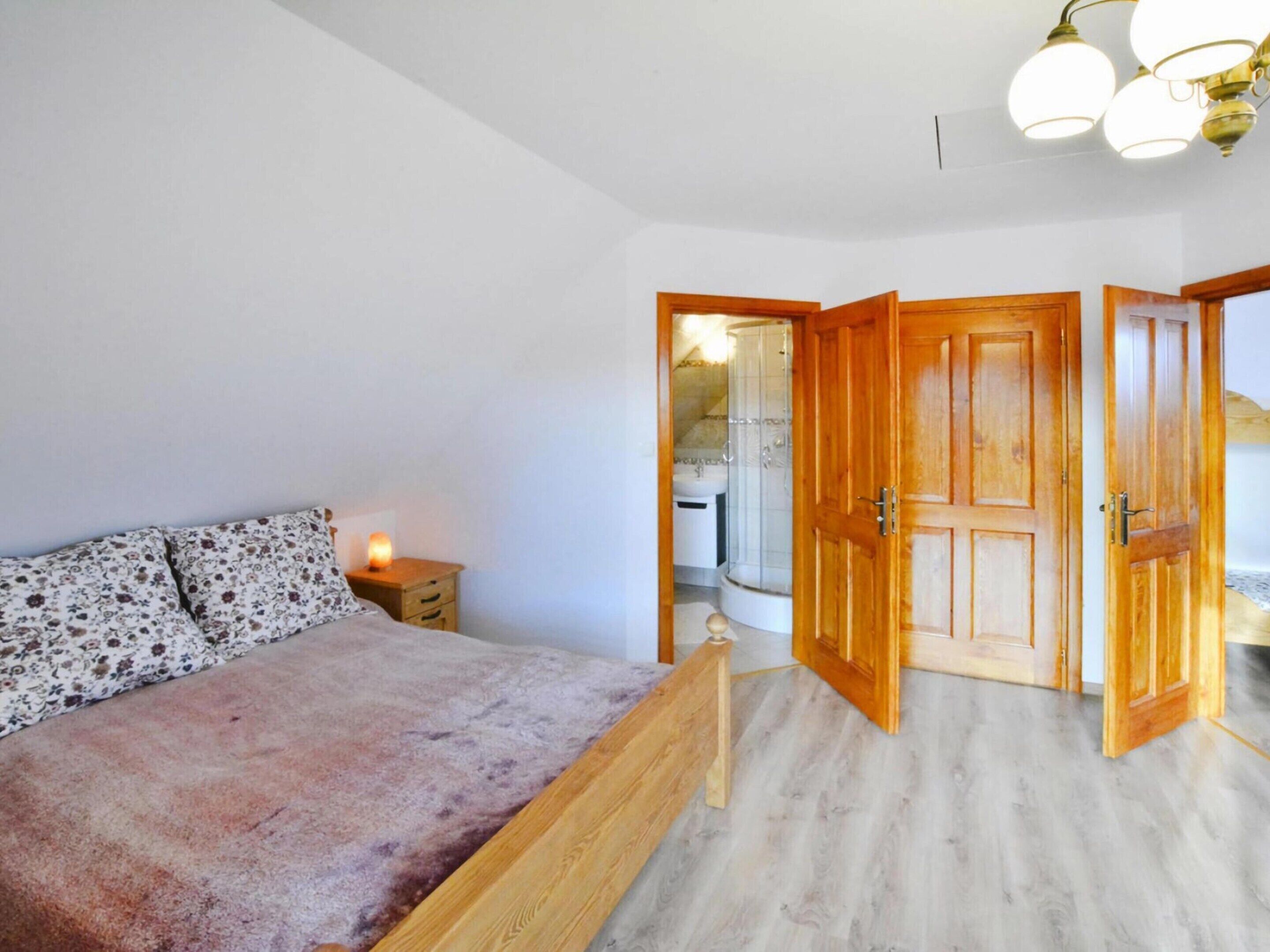 Un dormitorio con cama, mesita de noche y una puerta de madera que da a un baño.