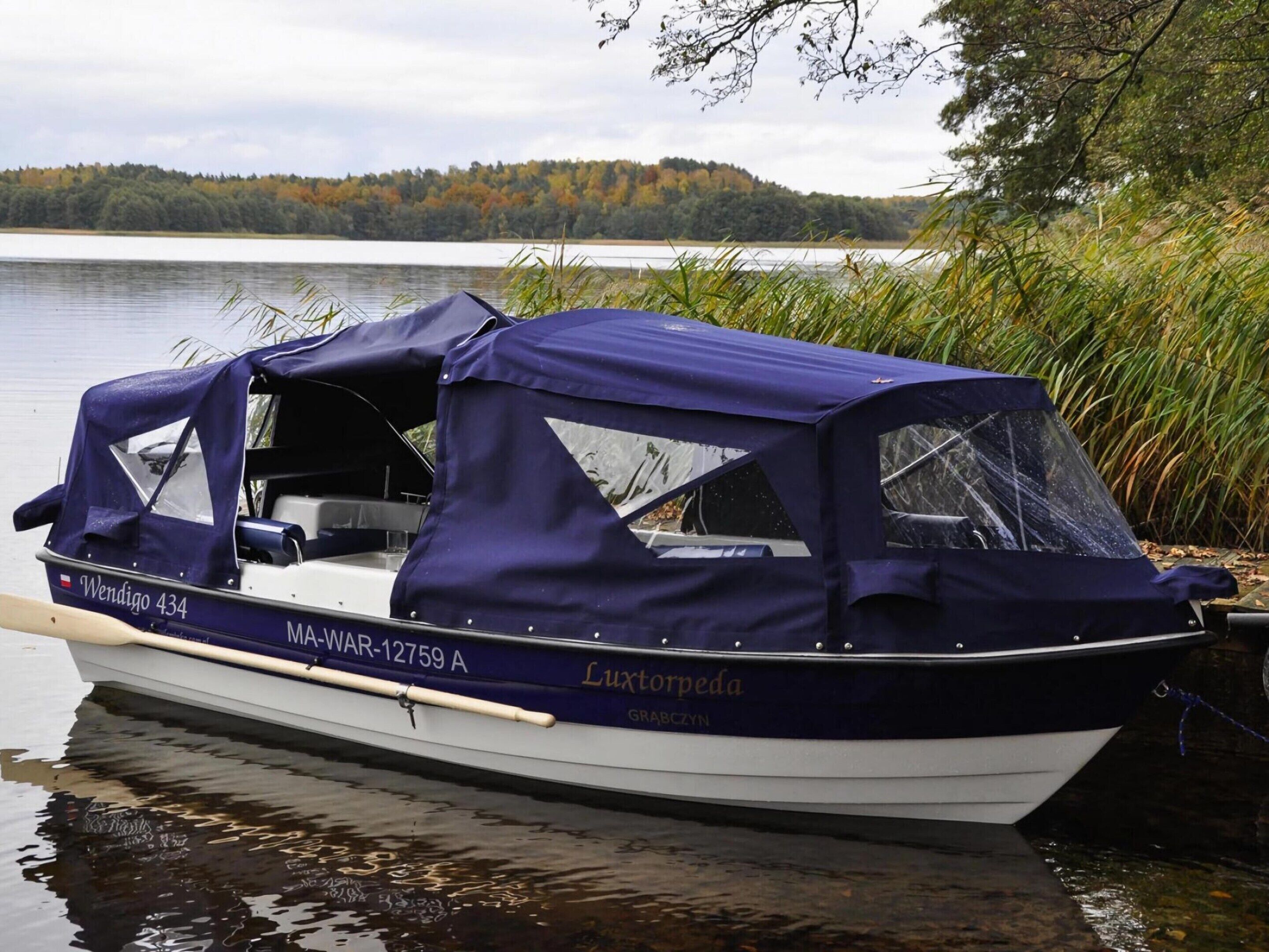 A boat named 'Wendigo 434' docked at a lake with a forested shoreline in the background.