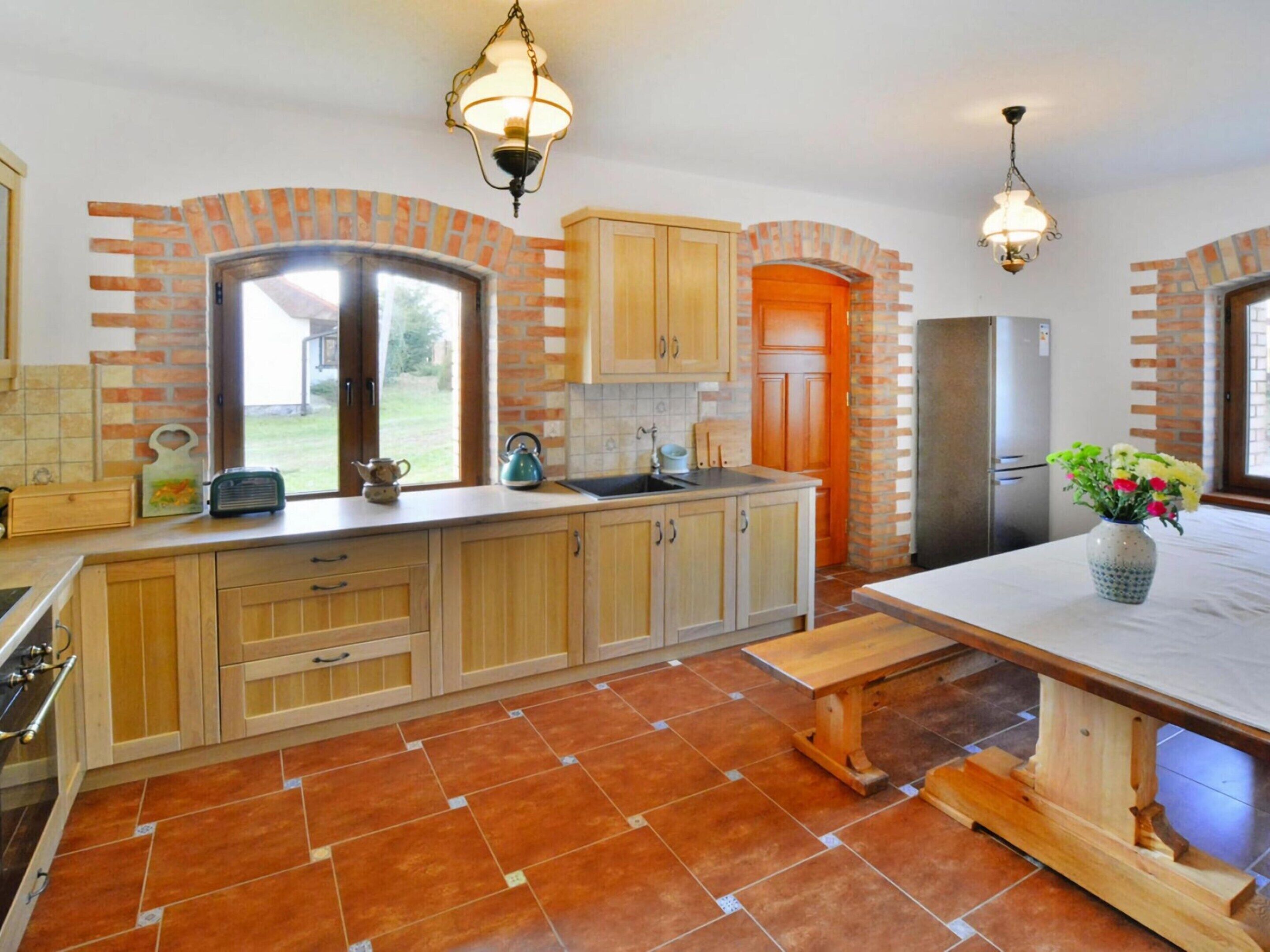 A kitchen with wooden cabinets, a tiled floor, a bench, and a refrigerator.