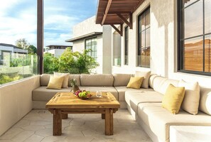 A modern outdoor seating area with a wooden table, beige sofa, and yellow cushions. - Nila Residence (Canggu)