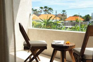 A balcony with two wooden chairs, a small table with a notebook and pen, and a view of houses and greenery. - Nila Residence (Canggu)