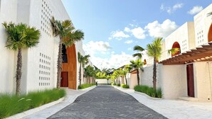 A paved pathway flanked by palm trees and buildings with a clear sky above. - Nila Residence (Canggu)