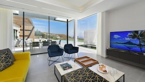 Una sala de estar moderna con un sofá amarillo, dos sillones azules, una mesa de centro de mármol y un televisor de pantalla plana grande.