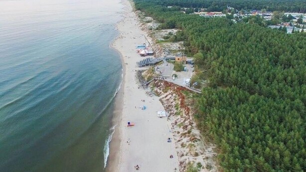 Une vue aérienne d’une plage, avec une zone boisée et des bâtiments en arrière-plan.