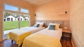 Une chambre avec deux lits, des murs en bois, une grande fenêtre et une vue sur les maisons à l’extérieur.
