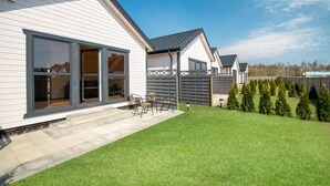 Une maison moderne dotée d’un patio, d’une pelouse et d’une rangée d’arbres à feuilles persistantes.