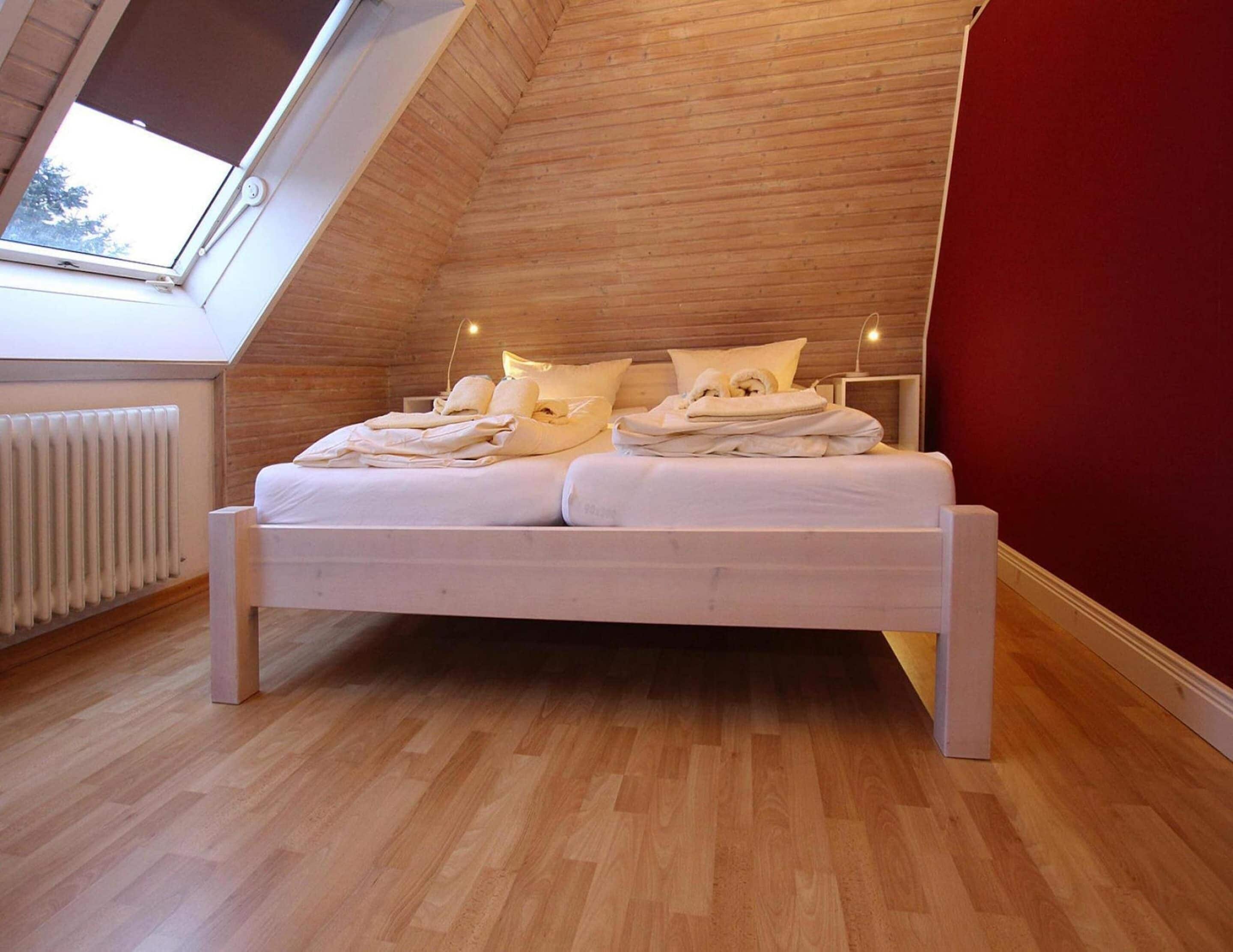 Een slaapkamer met een schuine kap, een bed met witte beddengoed, een radiator en een raam.
