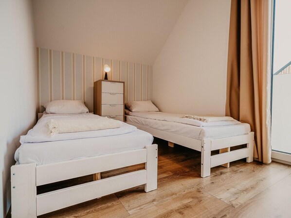 Une chambre à coucher avec deux lits blancs, une commode en bois et un mur à rayures.