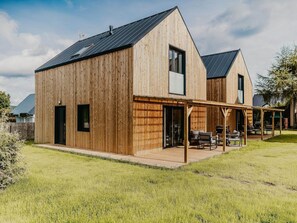 A modern wooden house with a large patio area, a covered outdoor seating area, and a visible chimney. - House in Nadole With Private Beach & Jacuzzi (Gniewino)