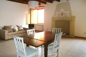 A living room with a wooden dining table, white chairs, a beige sofa, a television, and a fireplace. - Apartment in Lazise With Parking Space (Lazise)