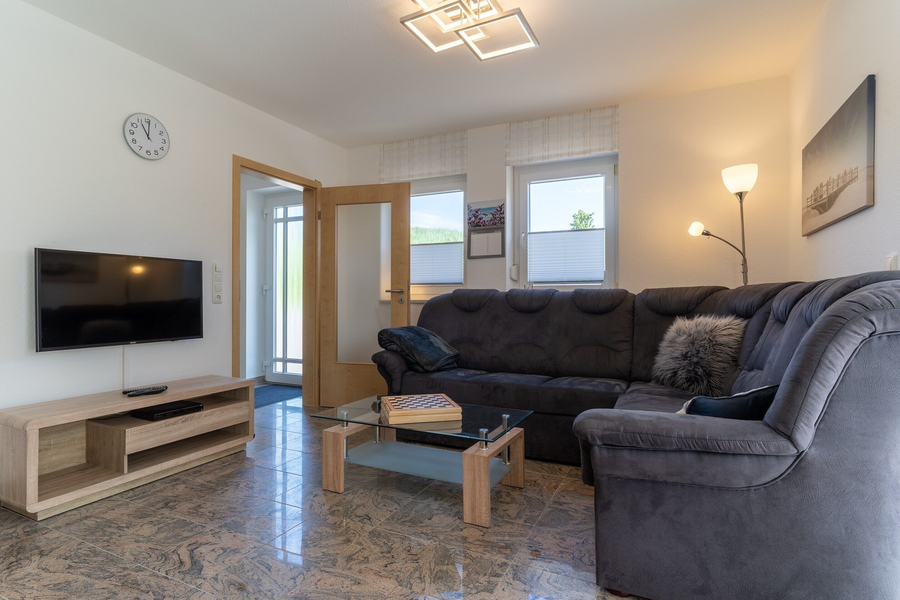 A modern living room with a flat-screen TV, a glass coffee table, a dark grey sofa, and a wooden entertainment unit.
