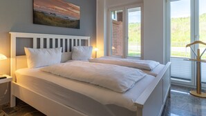 A bedroom with two beds, a painting on the wall, and a view of greenery through the window. - Wohnung in St.peter Ording (St. Peter-Ording)