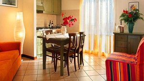 Zona pranzo con tavolo imbandito per quattro, divano, credenza e finestra con tende.