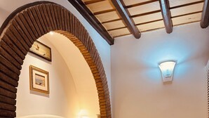 A bedroom with a large arched doorway, a bed with a headboard, a bedside table, a lamp, and a wall-mounted light fixture. - Loft Apartment Termini Colosseum (Roma)