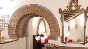 A room with a brick archway leading to a bed, a large ornate mirror, and a wooden table with a silver bowl. - Loft Apartment Termini Colosseum (Roma)