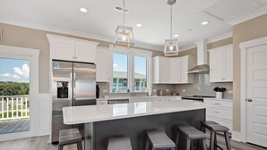 A modern kitchen with white cabinets, a large island with bar stools, stainless steel appliances, and pendant lighting. - A New Hope: Ocean View with Private Pool and Easy Beach Access (Oak Island)