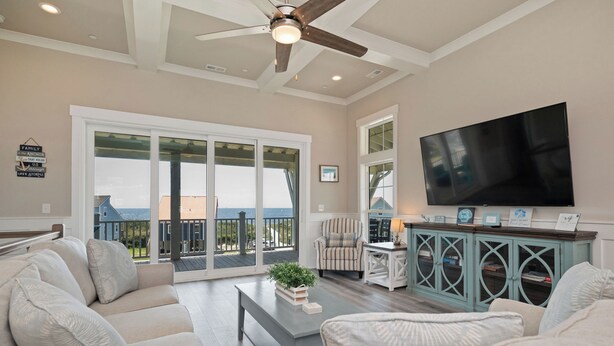 A spacious living room with a large TV, comfortable seating, a balcony with a view, and a ceiling fan. - A New Hope: Ocean View with Private Pool and Easy Beach Access (Oak Island)