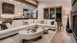 A modern living room with a sectional sofa, a round coffee table, and a kitchen in the background. - 1060 Park Ski Magnificent Mountain Retreat 5 Bedroom Home by RedAwning (Park City)