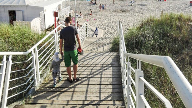 A staircase leading to a beach with a white railing, a person with a child, and a tent in the background. - Bungalow in Kolczewo Near Baltic Sea Beach (gmina Wolin)