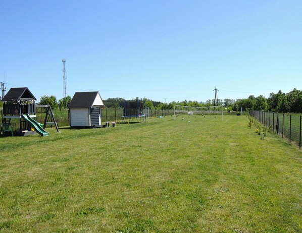 A grassy field with a playground, a small shed, and a fenced area.