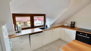 A modern kitchen with white cabinets, a wooden countertop, a built-in dishwasher, and a window overlooking a red-roofed building. - Spacious Holiday Apartment With a Large Terrace (Kołobrzeg)