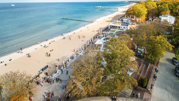 A beach with a pier extending into the sea, surrounded by trees and buildings. - Spacious Holiday Apartment With a Large Terrace (Kołobrzeg)