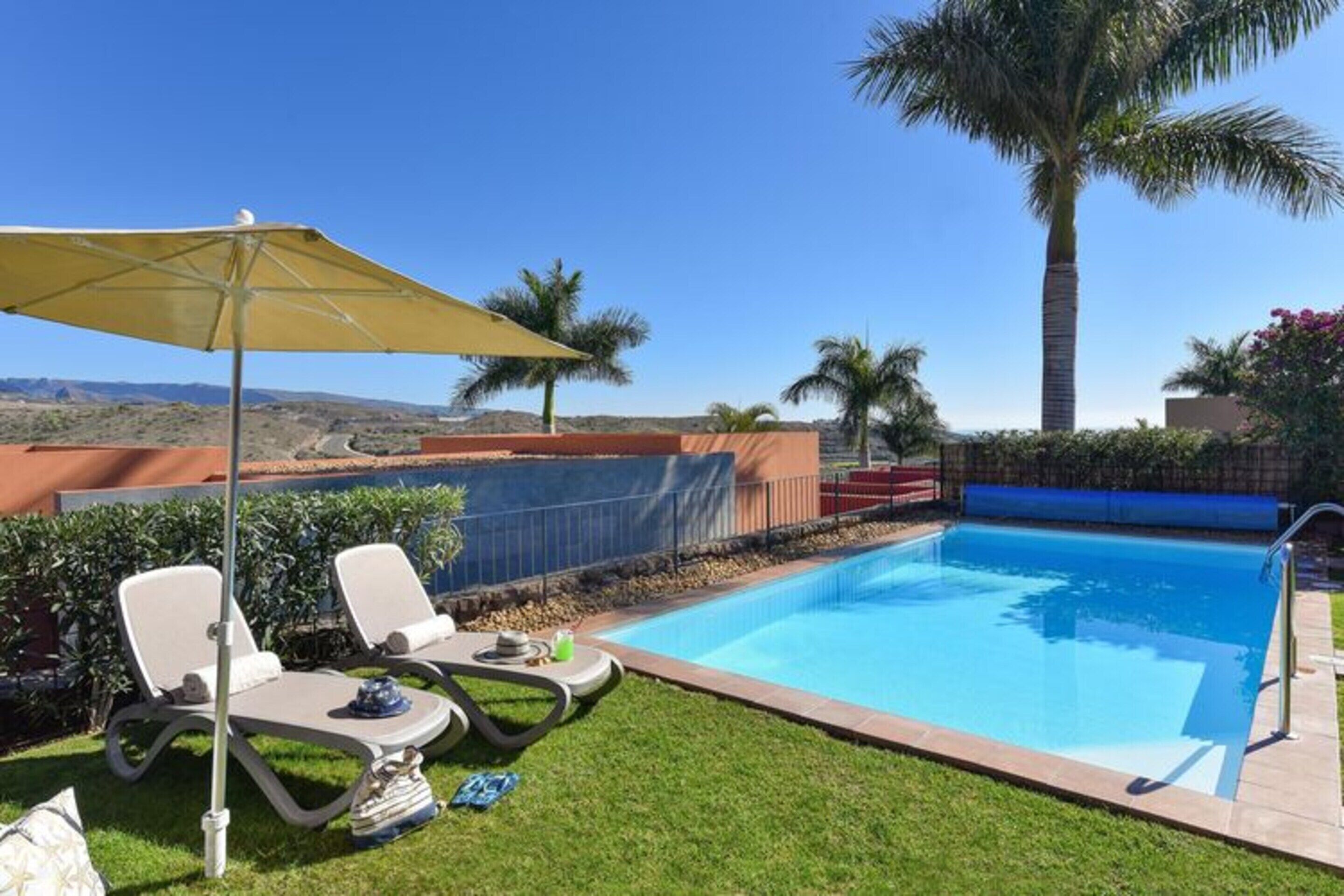 Une piscine dotée de chaises longues et d’un parasol, entourée de palmiers et offrant une vue sur le paysage.