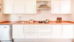 Una cocina con armarios blancos, un lavavajillas de acero inoxidable y un salpicadero de azulejos.