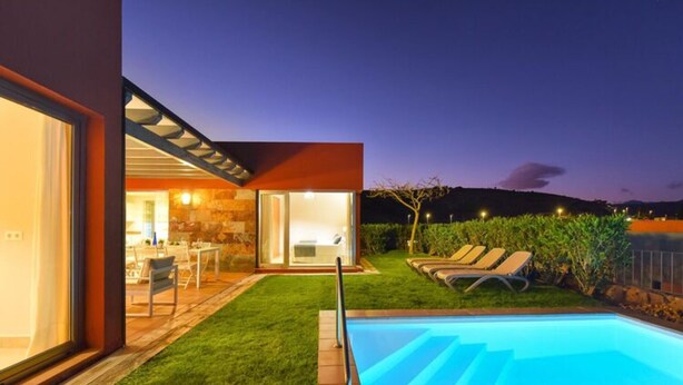 Una casa moderna con piscina, un patio con sillones de descanso y un interior luminoso.