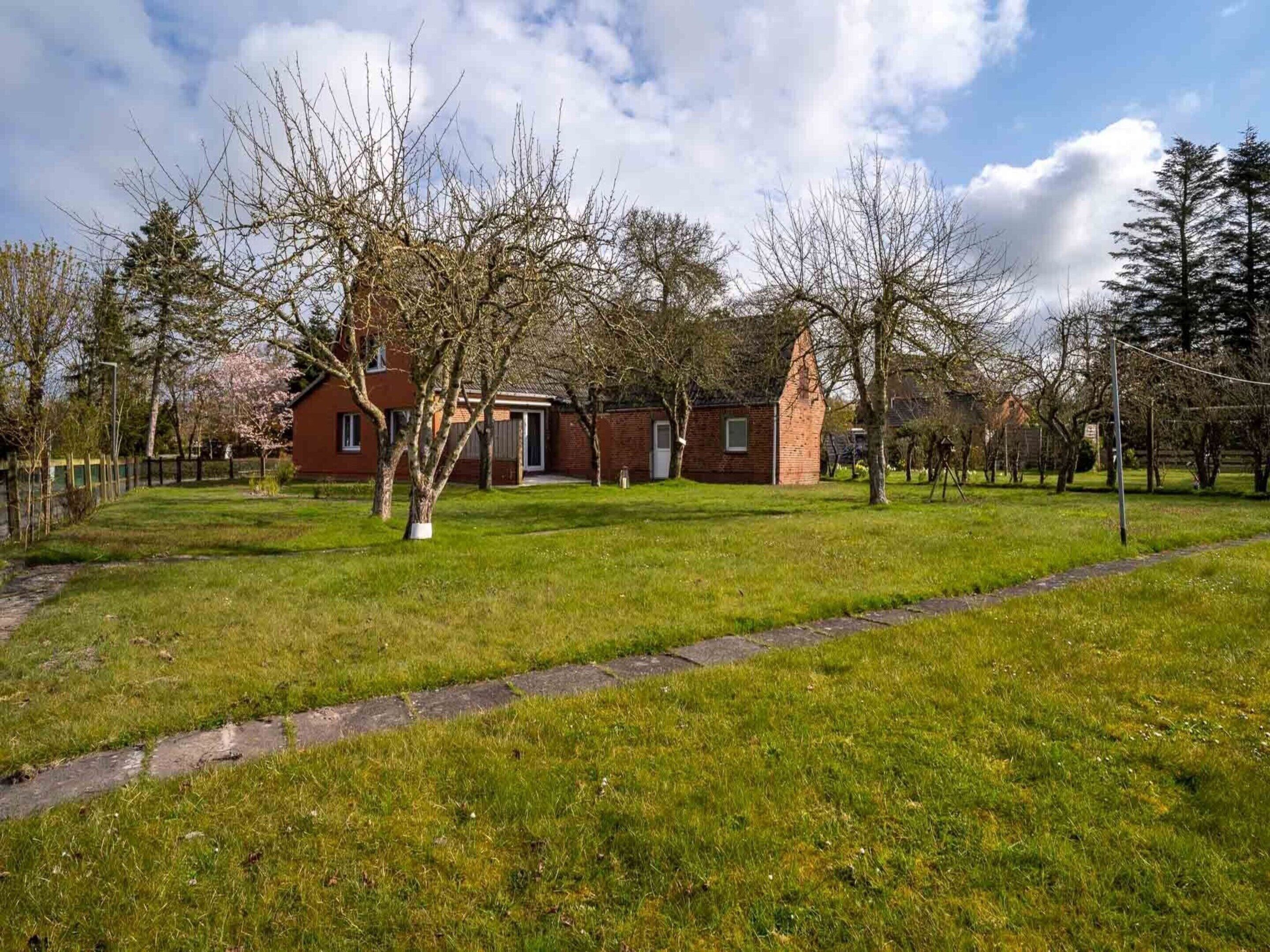 Ein Backsteinhaus mit roter Tür und einem kleinen Garten mit Gras und Bäumen.