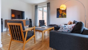 A modern living room with a sofa, a wooden chair, a coffee table, a TV, and a painting on the wall. - Ferienhaus in Garding (Garding)