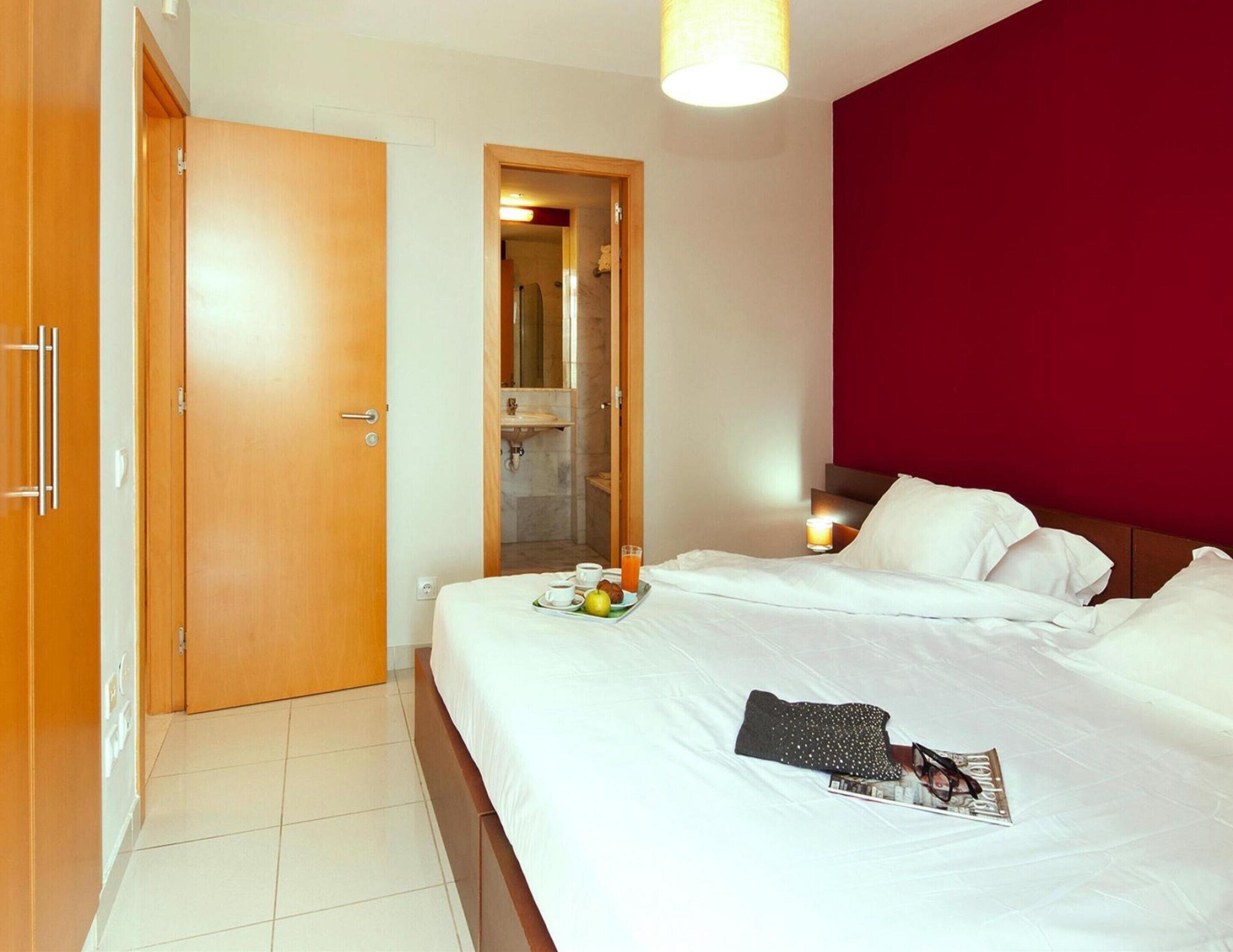 Une chambre d’hôtel avec un lit, une table de chevet, un miroir et une salle de bain visible à travers une porte ouverte.