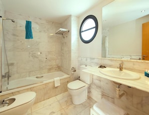 Ein modernes Badezimmer mit Badewanne, Toilette und Waschbecken, ausgestattet mit Marmorfliesen und einem runden Spiegel.