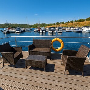 A deck with wicker furniture and a lifebuoy, overlooking a marina with boats. - Hausboot Junior am Geiseltalsee, Braunsbreda (Braunsbedra)