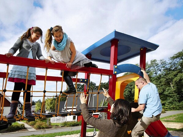 A playground with a red and yellow climbing structure, surrounded by greenery and a clear sky. - Appartements im Schlosspark Bad Saarow (Bad Saarow)