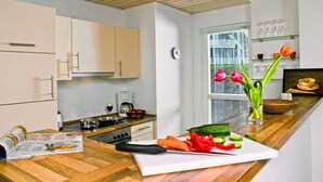 A modern kitchen with wooden cabinets, a stove, and a window with a view of a house. - Appartements im Schlosspark Bad Saarow (Bad Saarow)