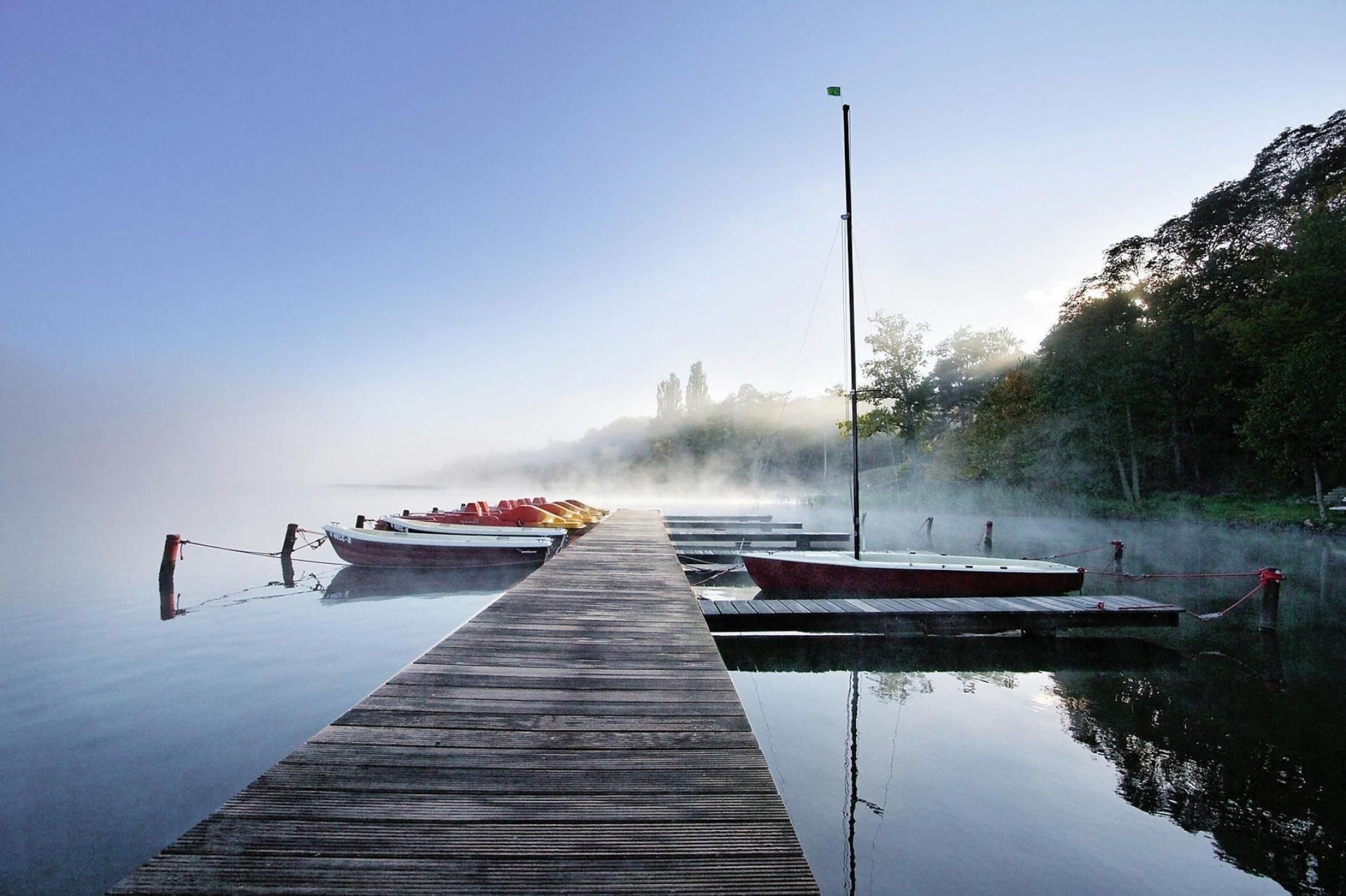 A wooden pier extending into calm water with boats docked at the end.