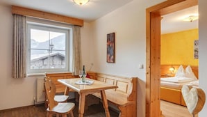 Un cuarto acogedor con una mesa y sillas de madera, una cama con cabecera y un ventanal con vistas a edificios.