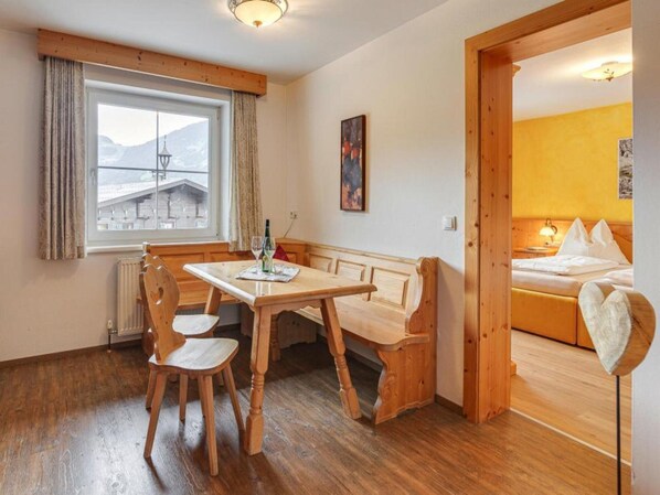 A cozy room with a wooden table and chairs, a bed with a headboard, and a window with a view of buildings.
