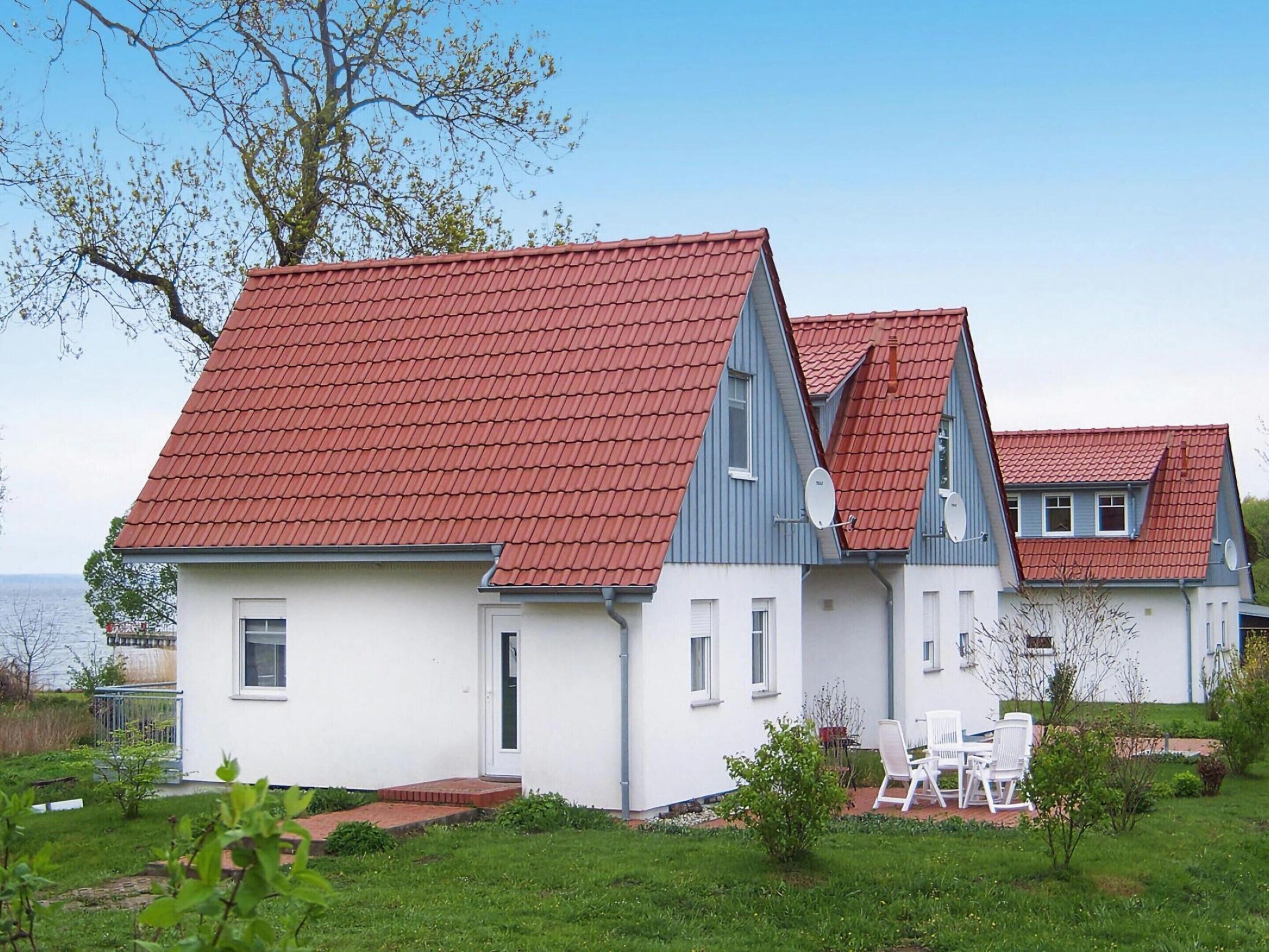 A two-story house with a red-tiled roof, white walls, and a small garden with outdoor furniture.