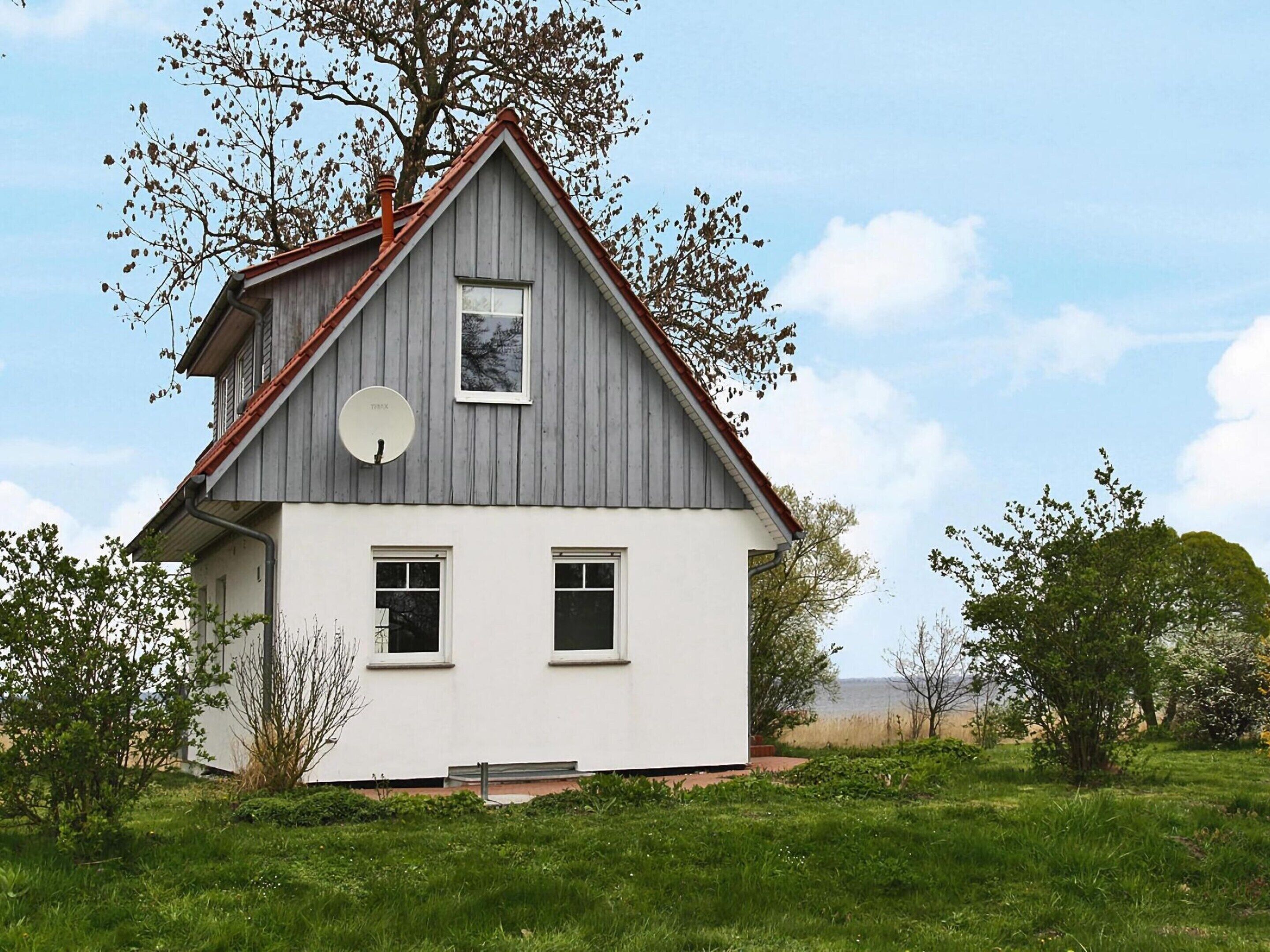 A two-story house with a gabled roof, a satellite dish, and a view of the sea.