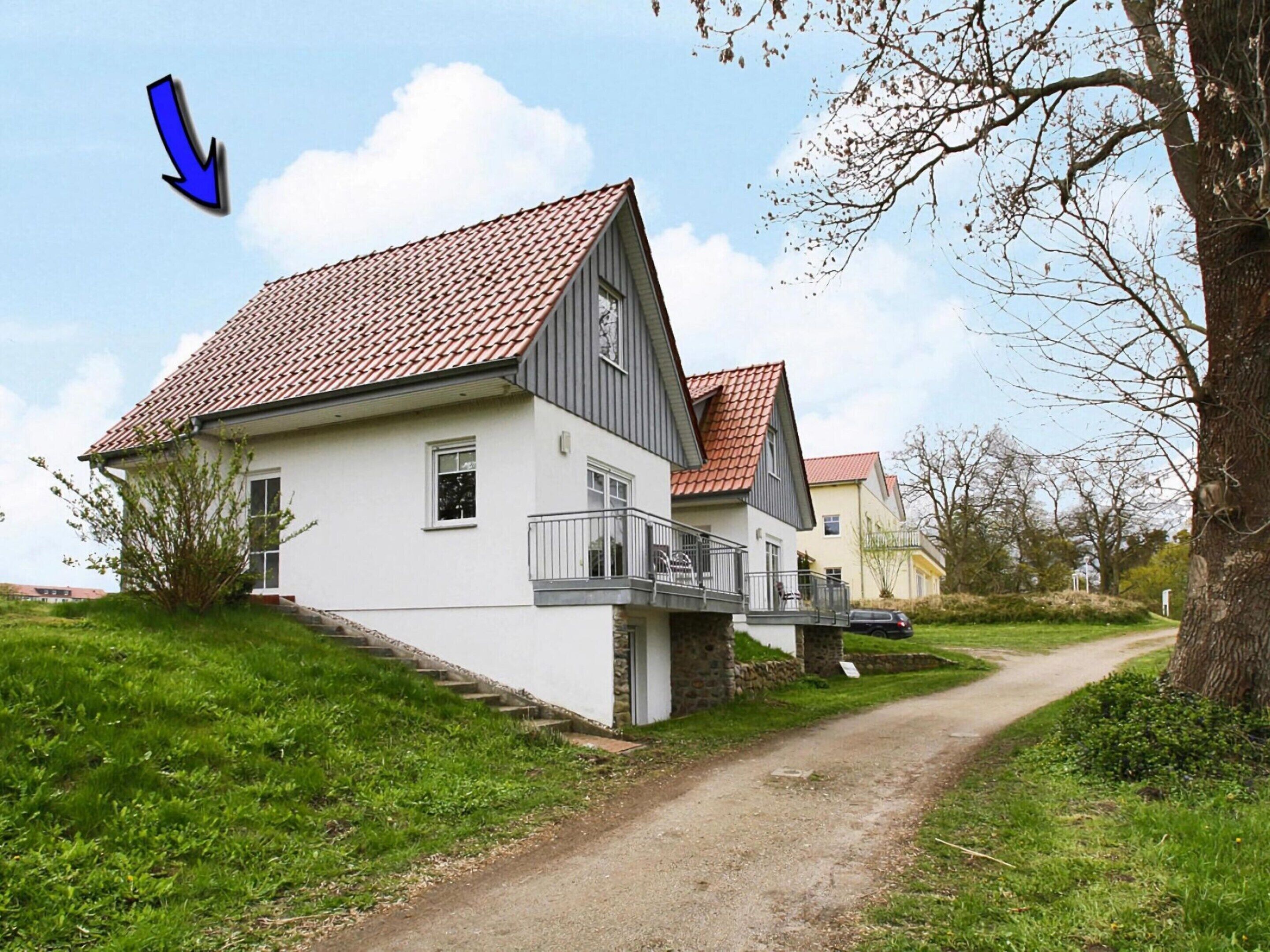 A two-story house with a red-tiled roof, a balcony, and a dirt path leading to it.