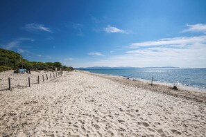 En sandstrand med ett staket, en bänk och en liten byggnad på vänster sida.